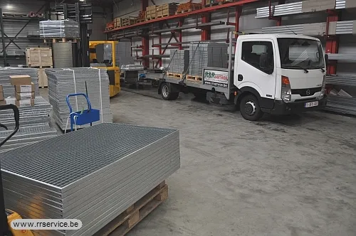 Magazijn met stapels gegalvaniseerde roosters op paletten en een bestelwagen