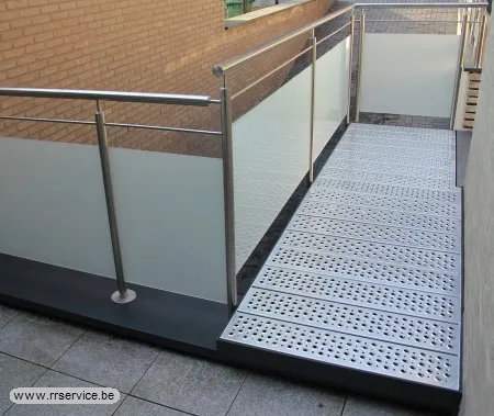 Loopbrug van geperforeerde metalen platen naast glazen balustrade met inox leuning